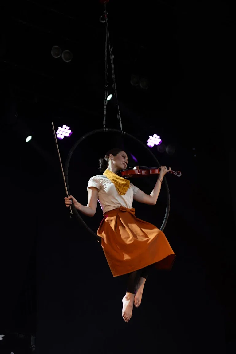 An aerial violinist suspended in a hoop under stage lights